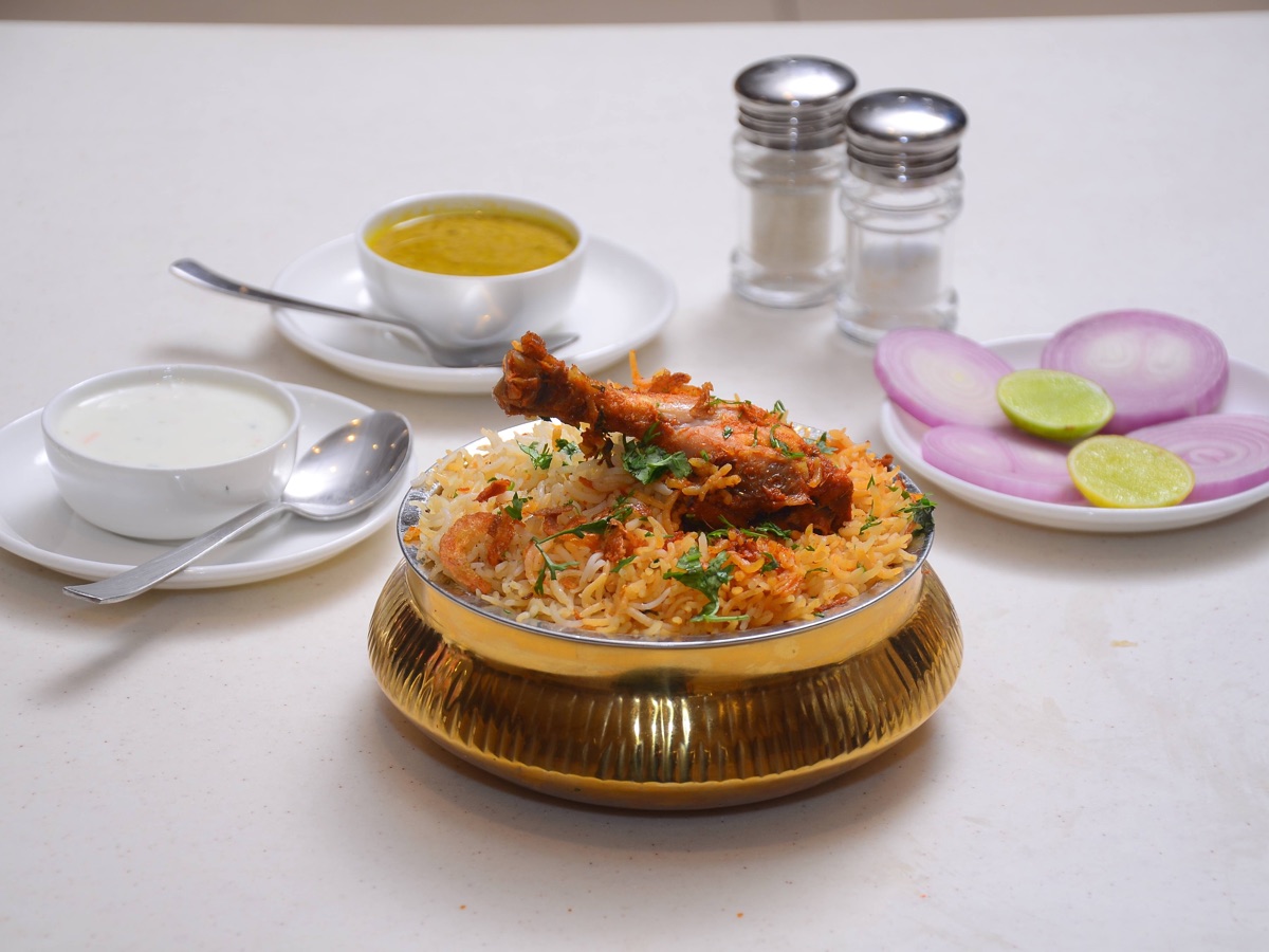 Sealed copper handi of dum biryani being opened, steam rising over saffron-streaked rice and mutton pieces